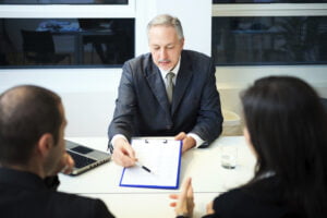 Andrew P. Gross, a senior businessman, reviews a document during a meeting with two other colleagues in a modern office.