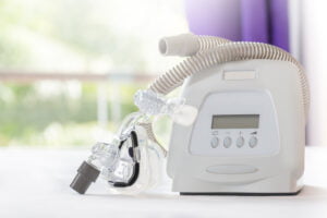 A CPAP machine with a face mask and hose on a table, used for treating sleep apnea, with Andrew P. Gross in the blurred background.