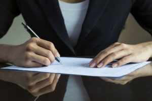 A person in a business suit signing a VA disability claim document on a desk.
