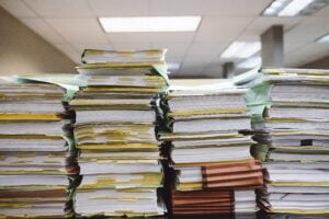 Large stacks of various colored files and paperwork piled high on Andrew P. Gross' desk in a VA office setting.
