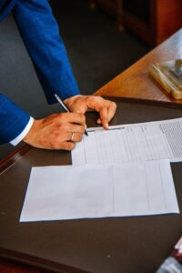 A person in a blue suit signs a VA disability rating document on a wooden desk, with a blank white paper beside the form.